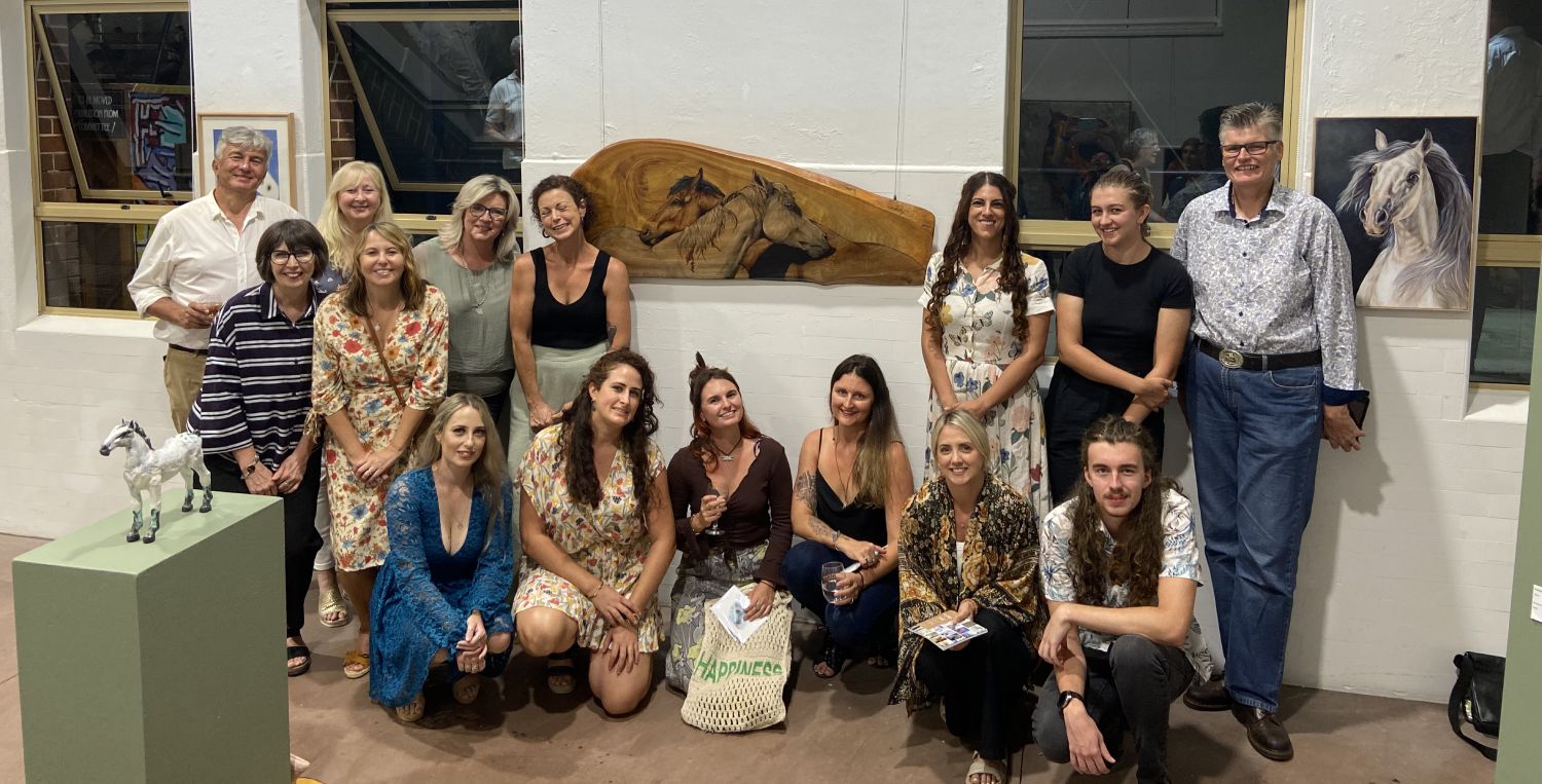 Some of the Hoofbeats volunteers and directors standing in front of a wall of horse artwork, at the opening of the Seeing the Soul art exhibition