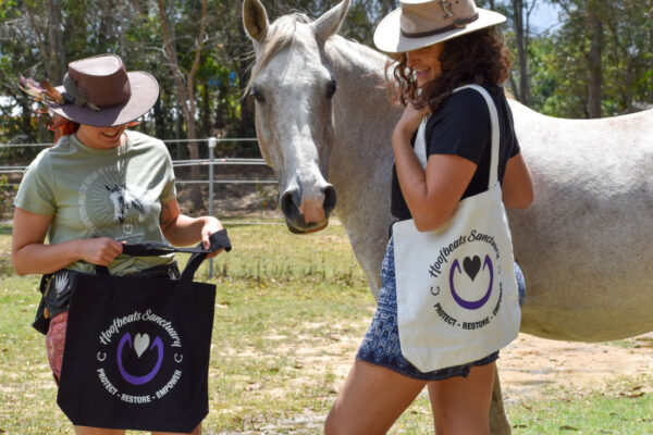 Two models posing with our Hoofbeats tote bags next to Kazu the horse