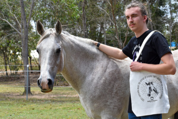 A model posing with one of our white coloured Hoofbeats tote bags, next to Kazu the horse