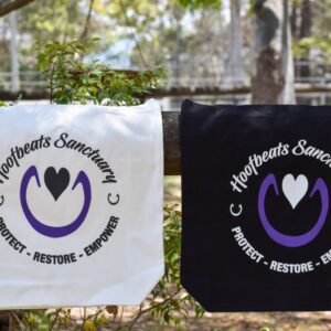 Our two tote bags with the Hoofbeats logo, in both white and black, strung along a railing.