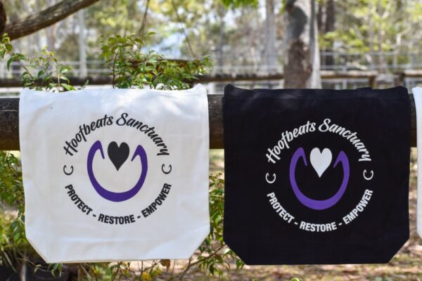 Our two tote bags with the Hoofbeats logo, in both white and black, strung along a railing.